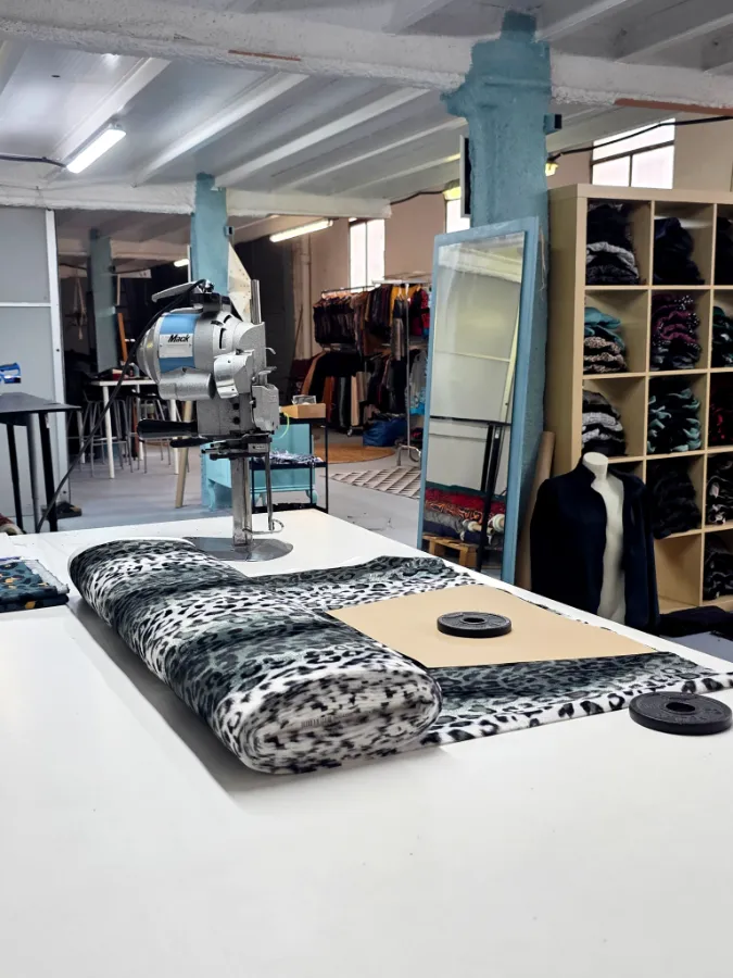 The workshop cutting table with a rolled animal-print fabric, a fabric cutting machine and a mirror with a blue frame.